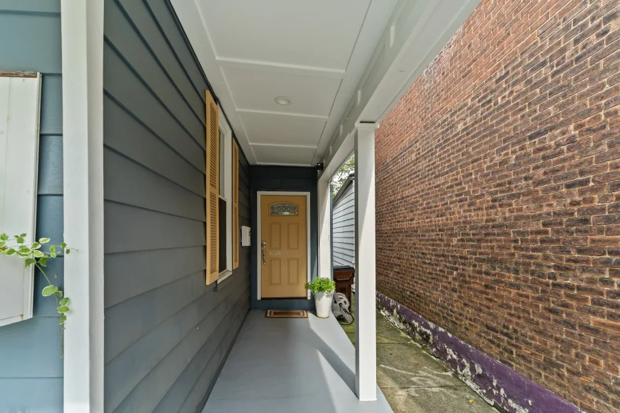 Covered front porch with wood shutters, hanging ferns, and a yellow front door — photographed by 513Shutter Cincinnati