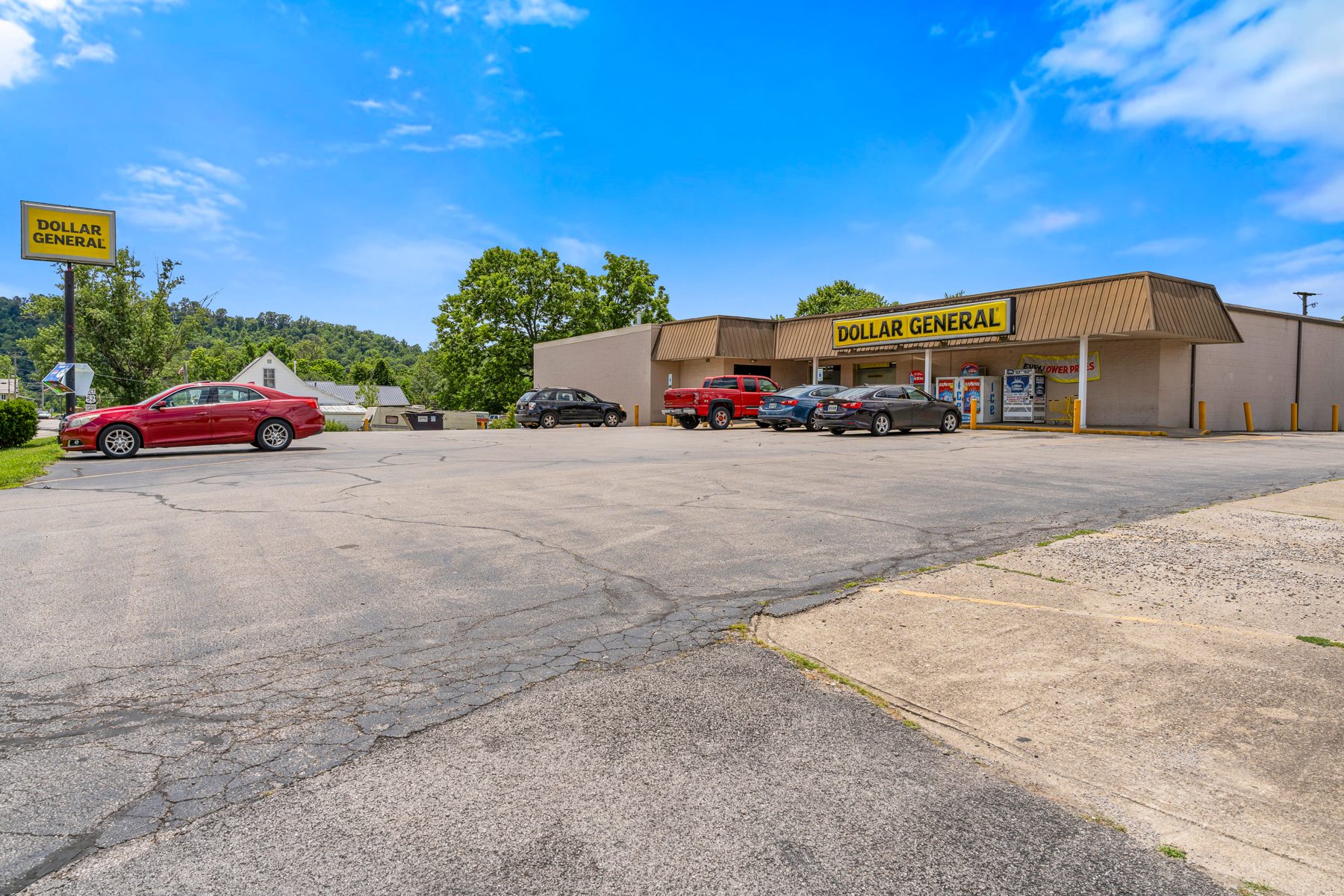 Wide street view of the Dollar General building and parking lot with pylon sign in the distance
