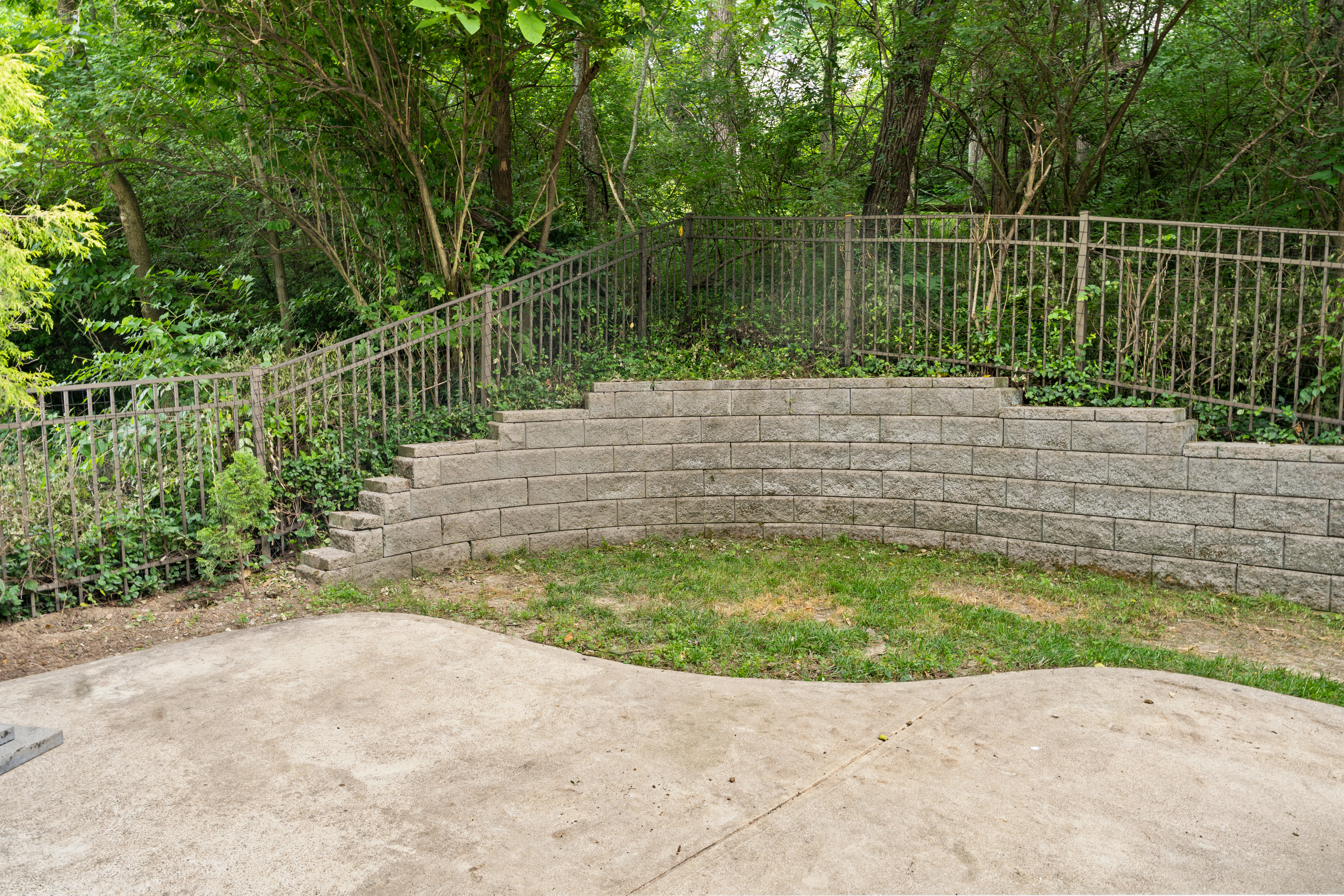 Backyard retaining wall with tiered garden beds, iron railing, and wooded backdrop