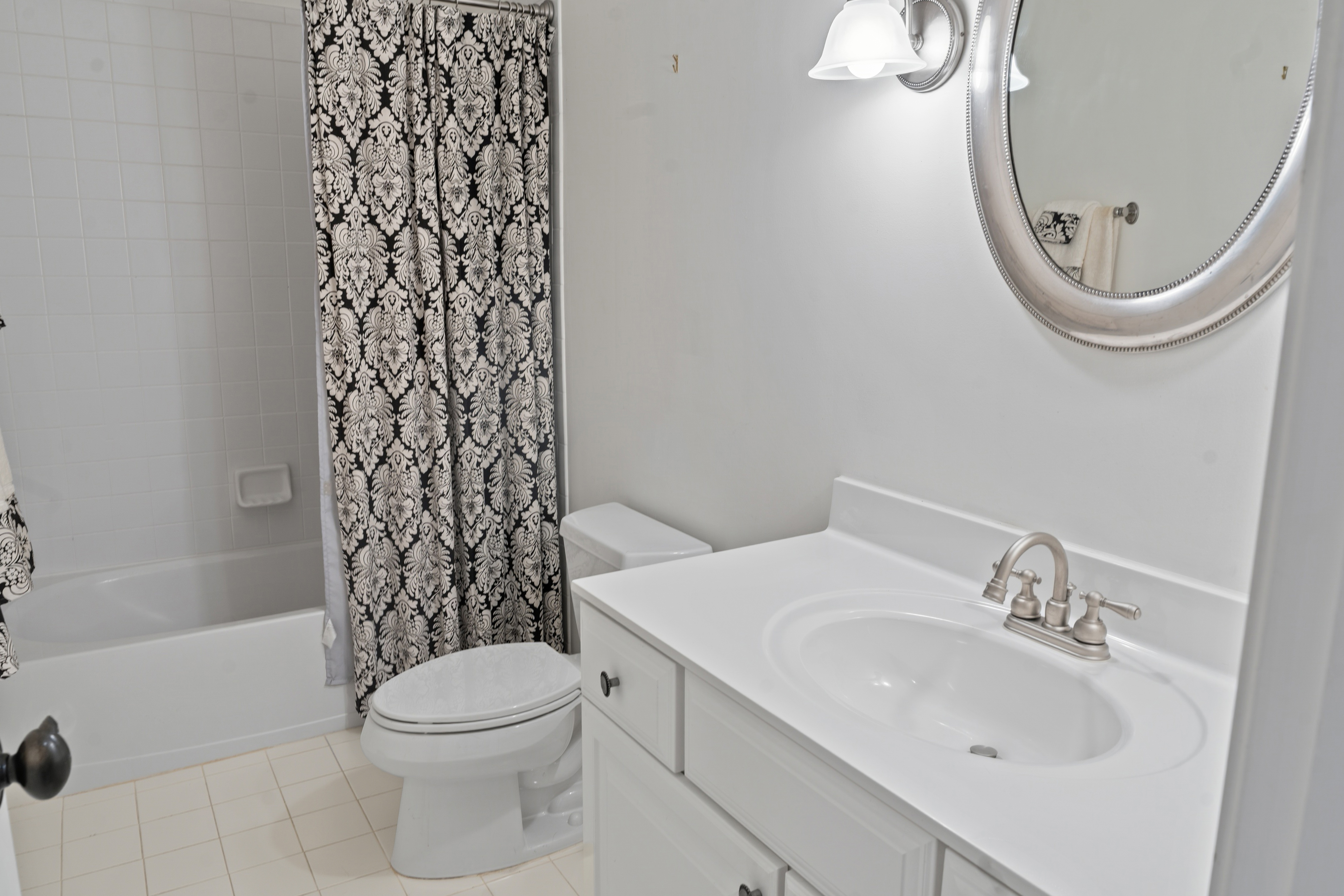Full bathroom with tub-shower combo, patterned curtain, white vanity, and round decorative mirror