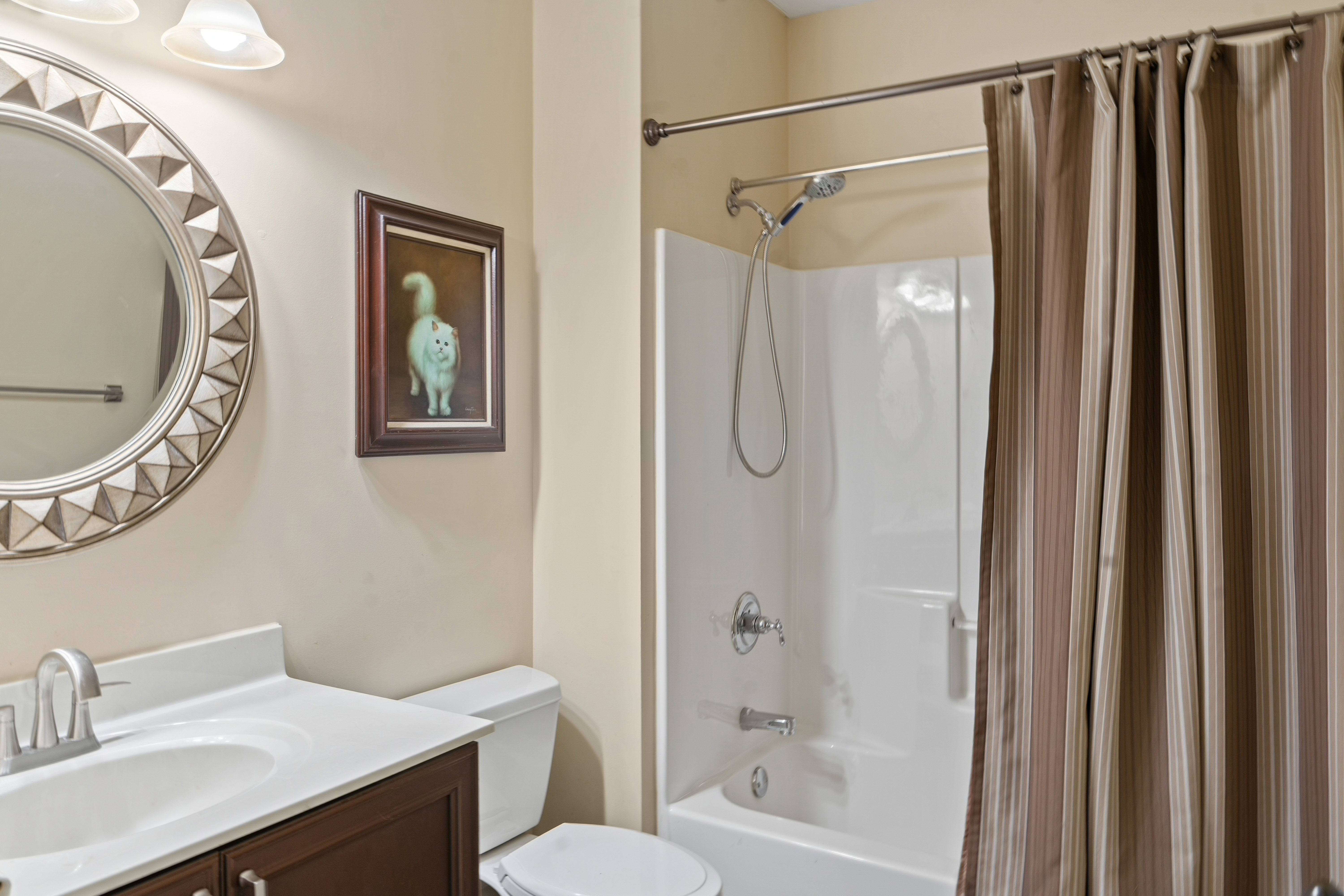 Bathroom with tub-shower combo, striped curtain, dark wood vanity, and sunburst round mirror