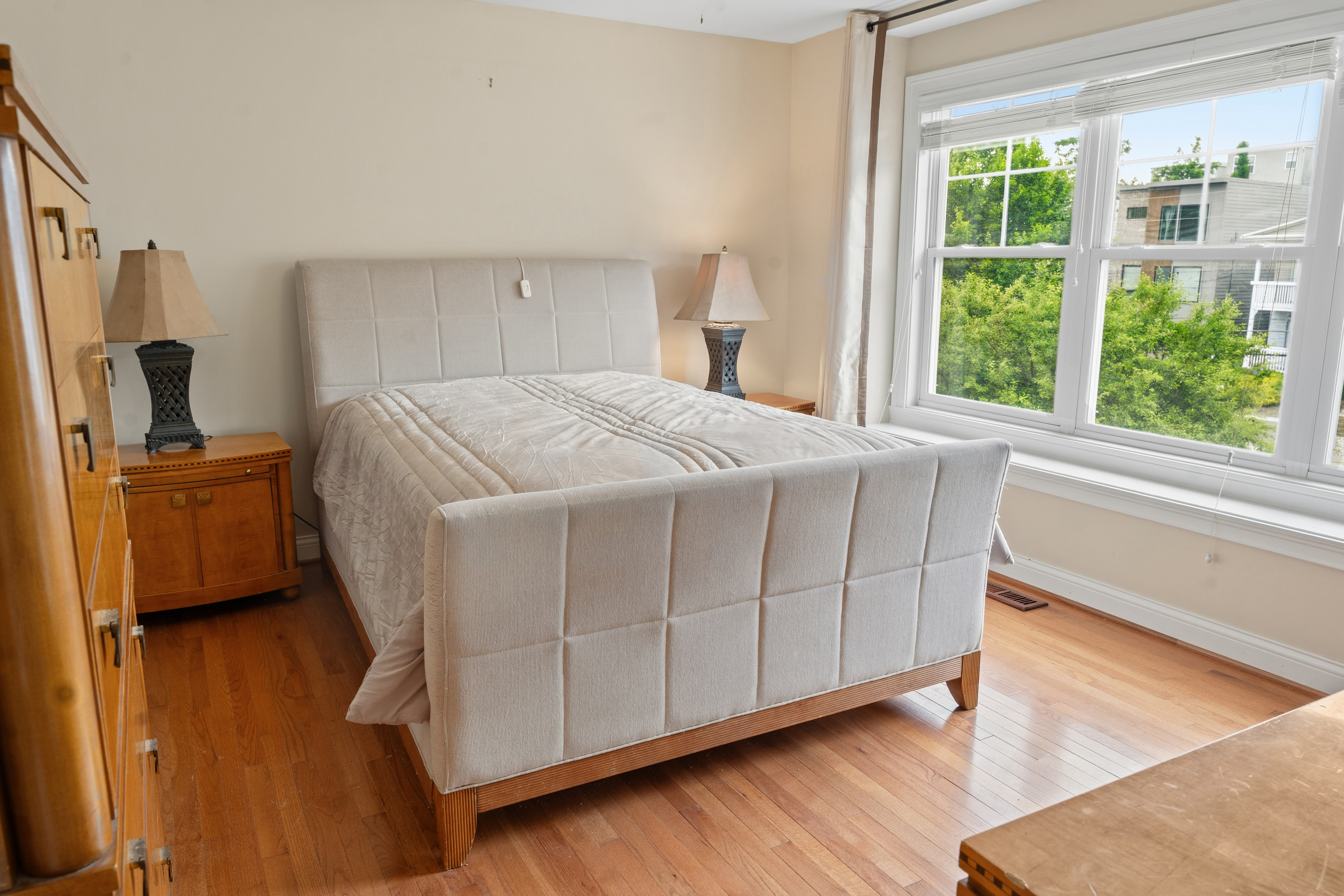 Secondary bedroom with upholstered queen bed, wood floors, and bright double windows