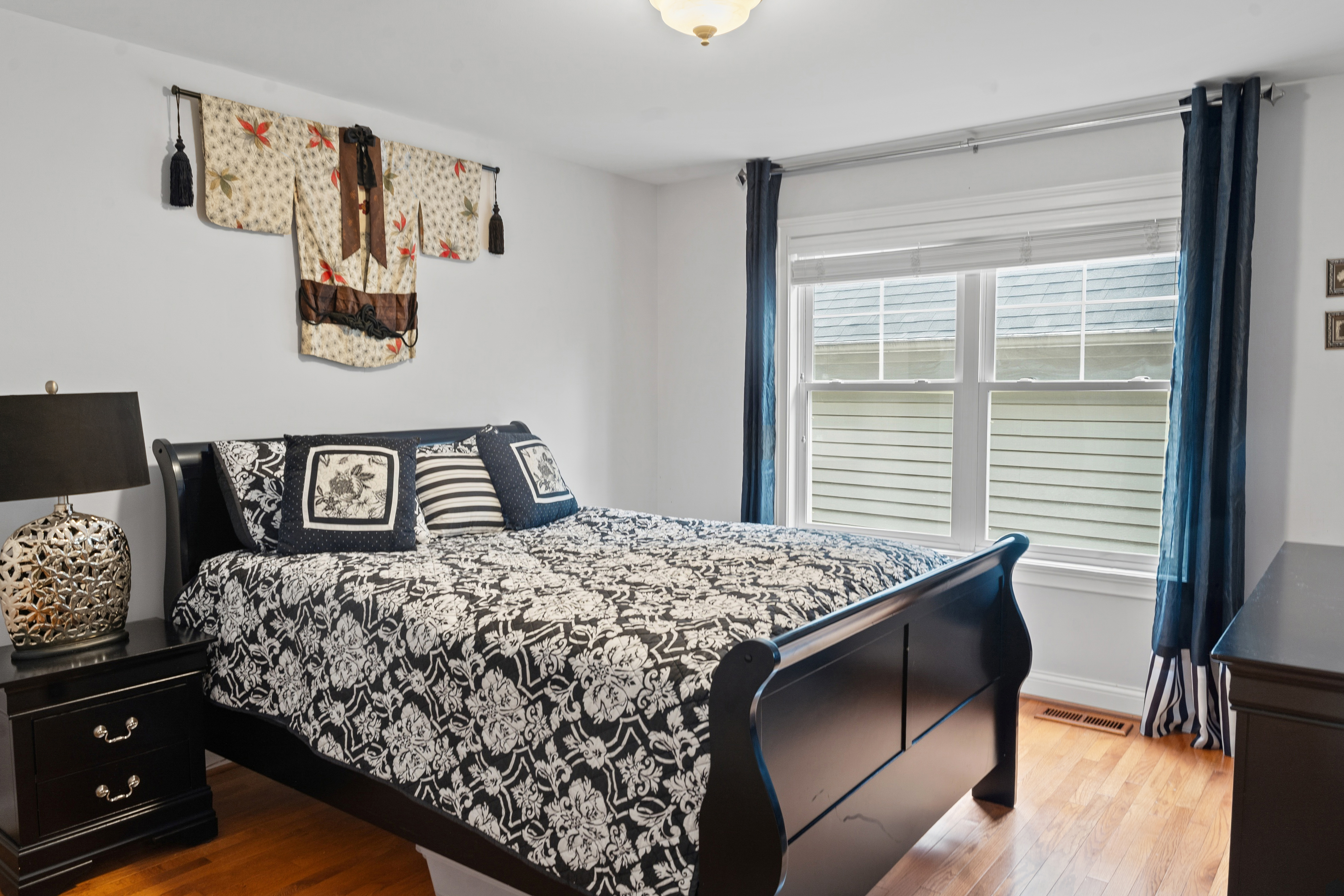 Bedroom with dark sleigh bed, blue drapes, decorative kimono wall art, and hardwood floors