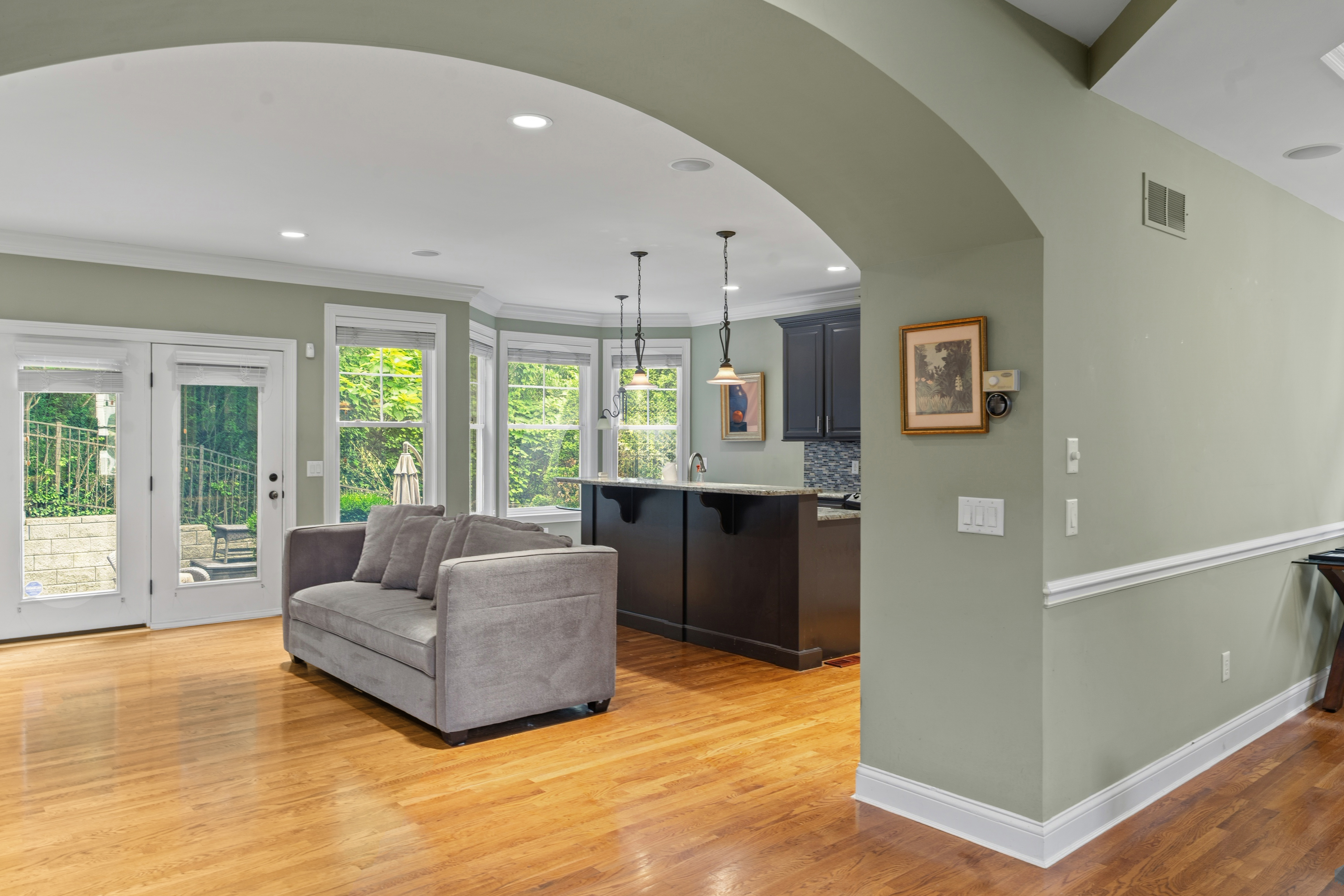 Open family room and kitchen view through arched doorway showing sofa, French doors, and kitchen island