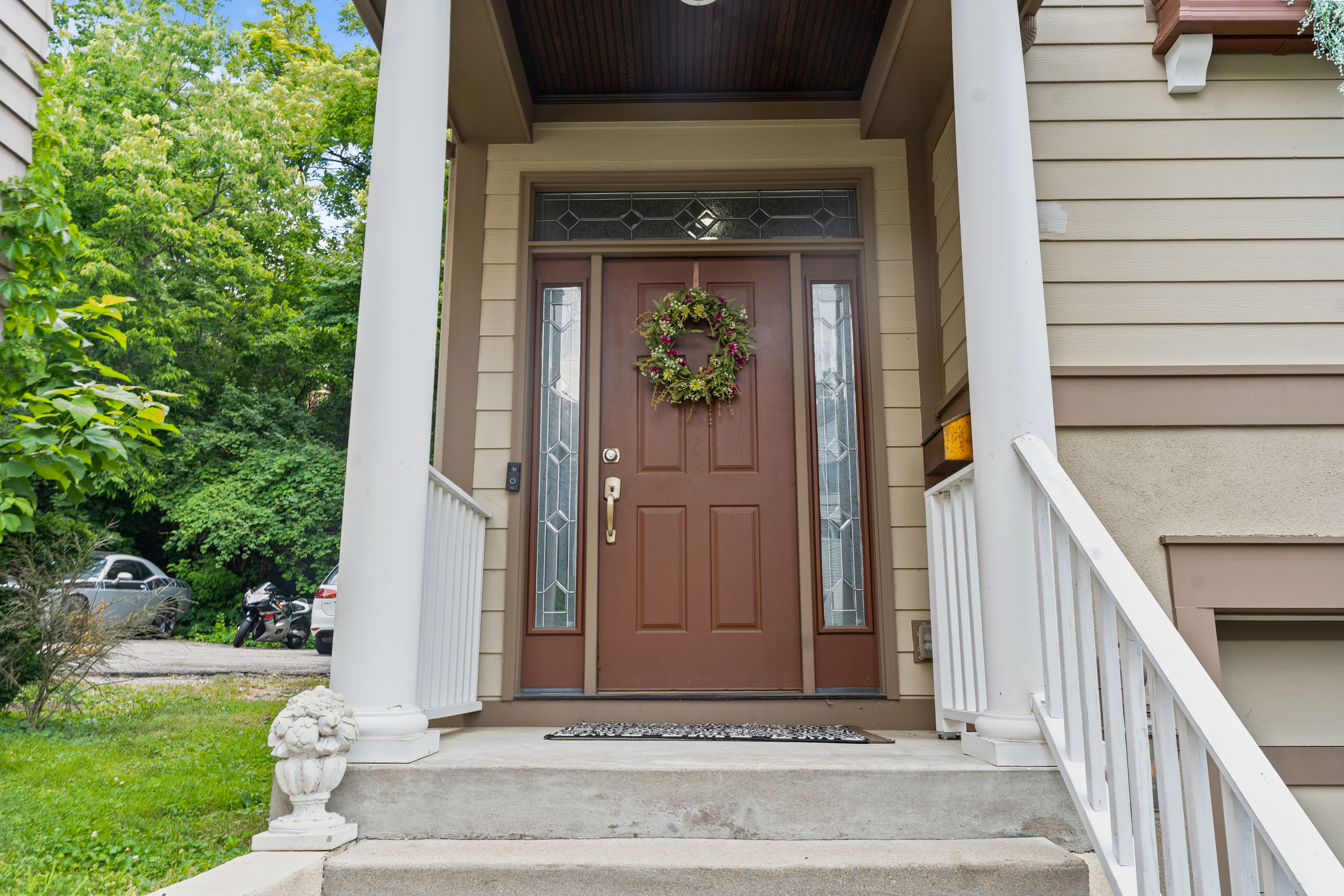 Close-up of the front door entry with decorative wreath, leaded glass sidelights, and covered front porch