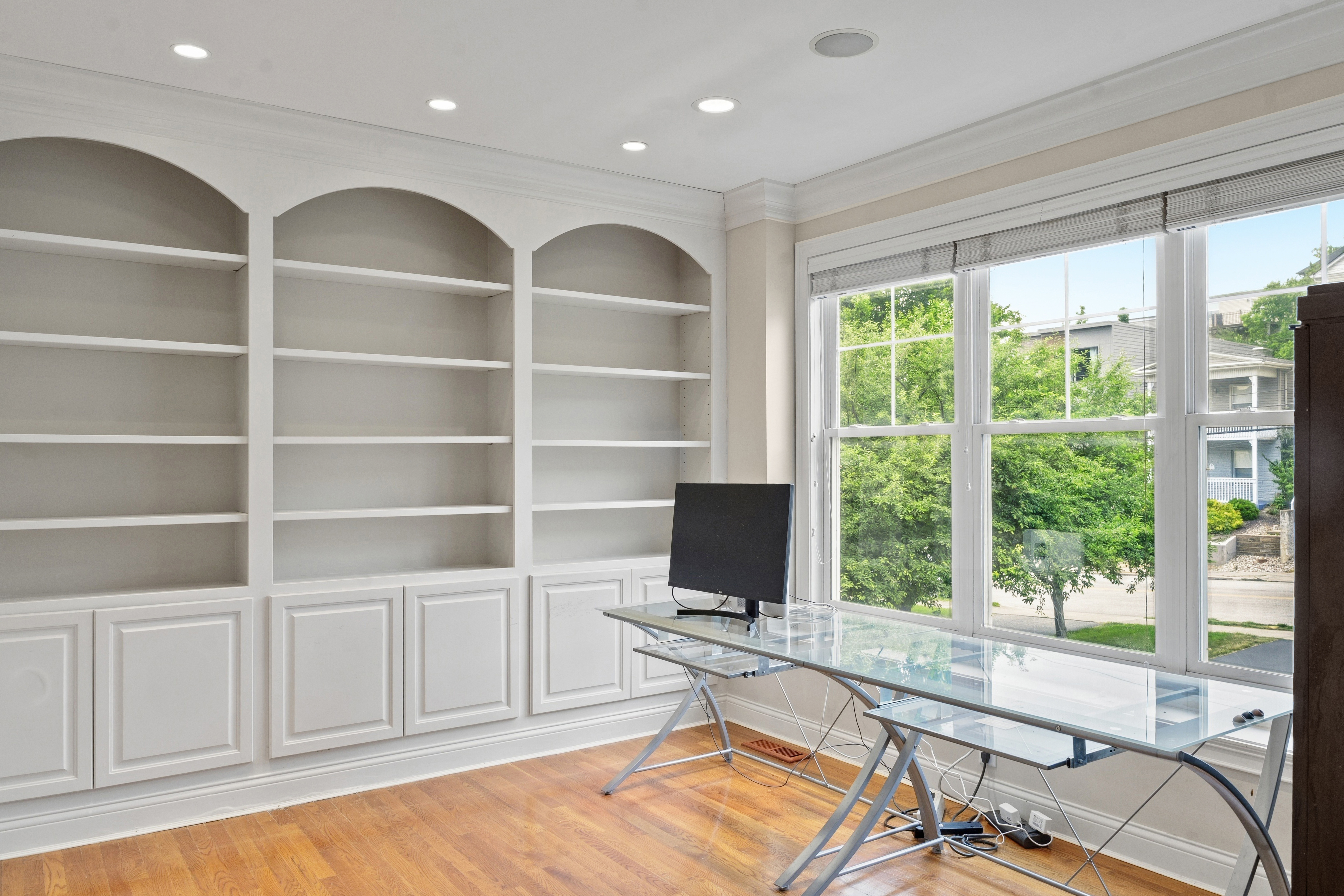 Home office with floor-to-ceiling built-in shelving, glass desk, and large windows overlooking the yard