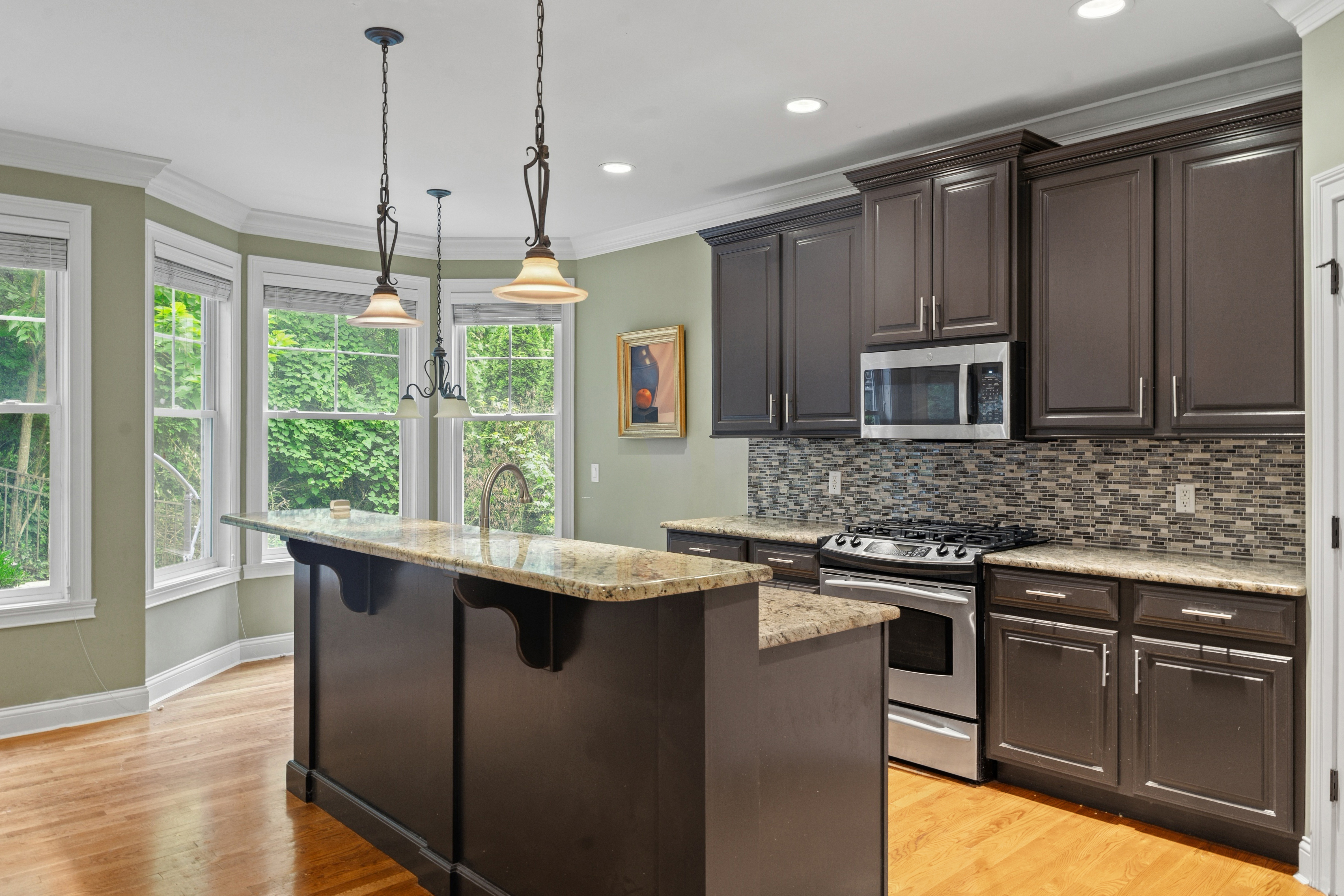Kitchen with bay window seating area, dark cabinetry, granite island, and pendant lighting