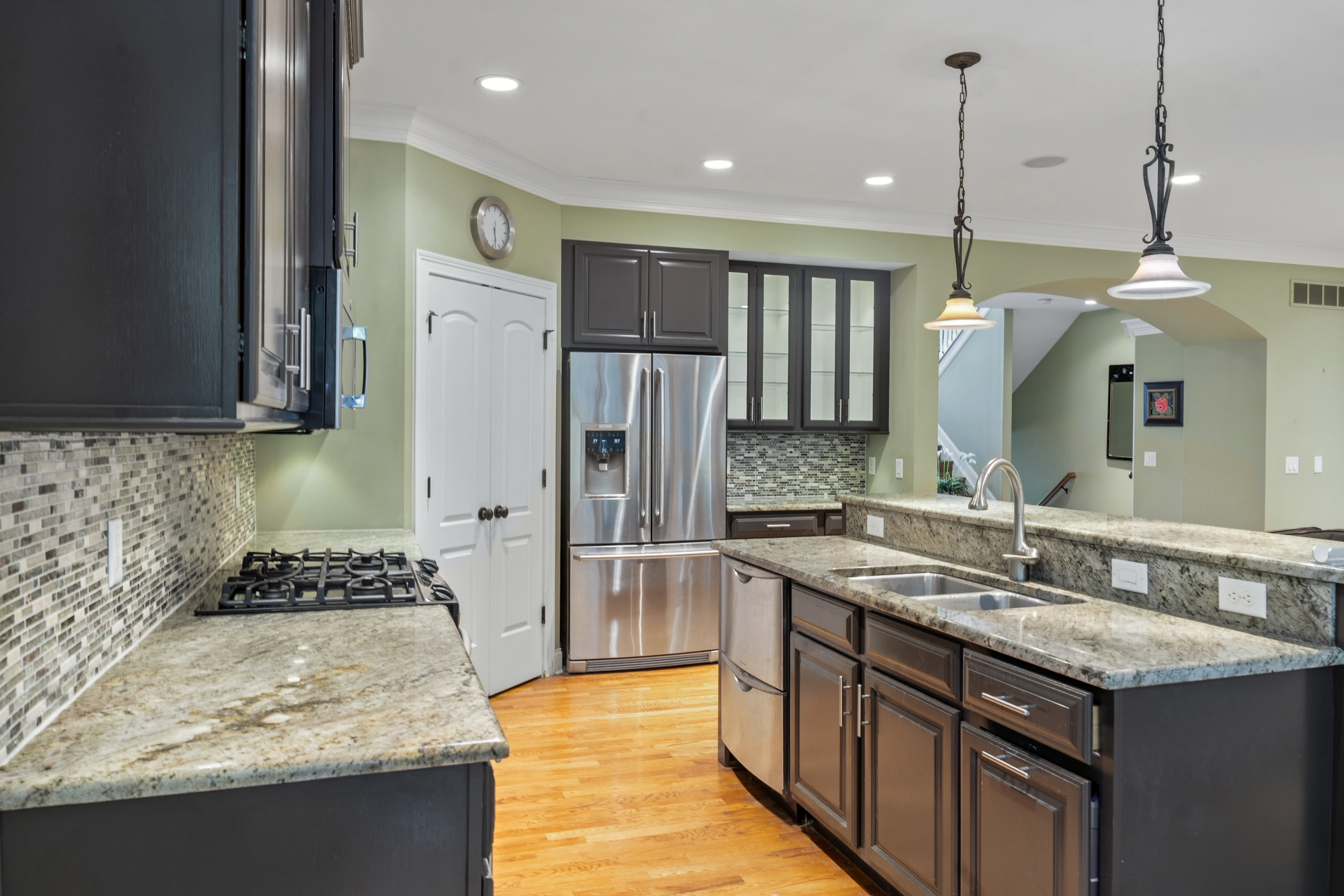 Kitchen from cooking side showing gas cooktop, stainless refrigerator, dark cabinetry, and arched view to family room