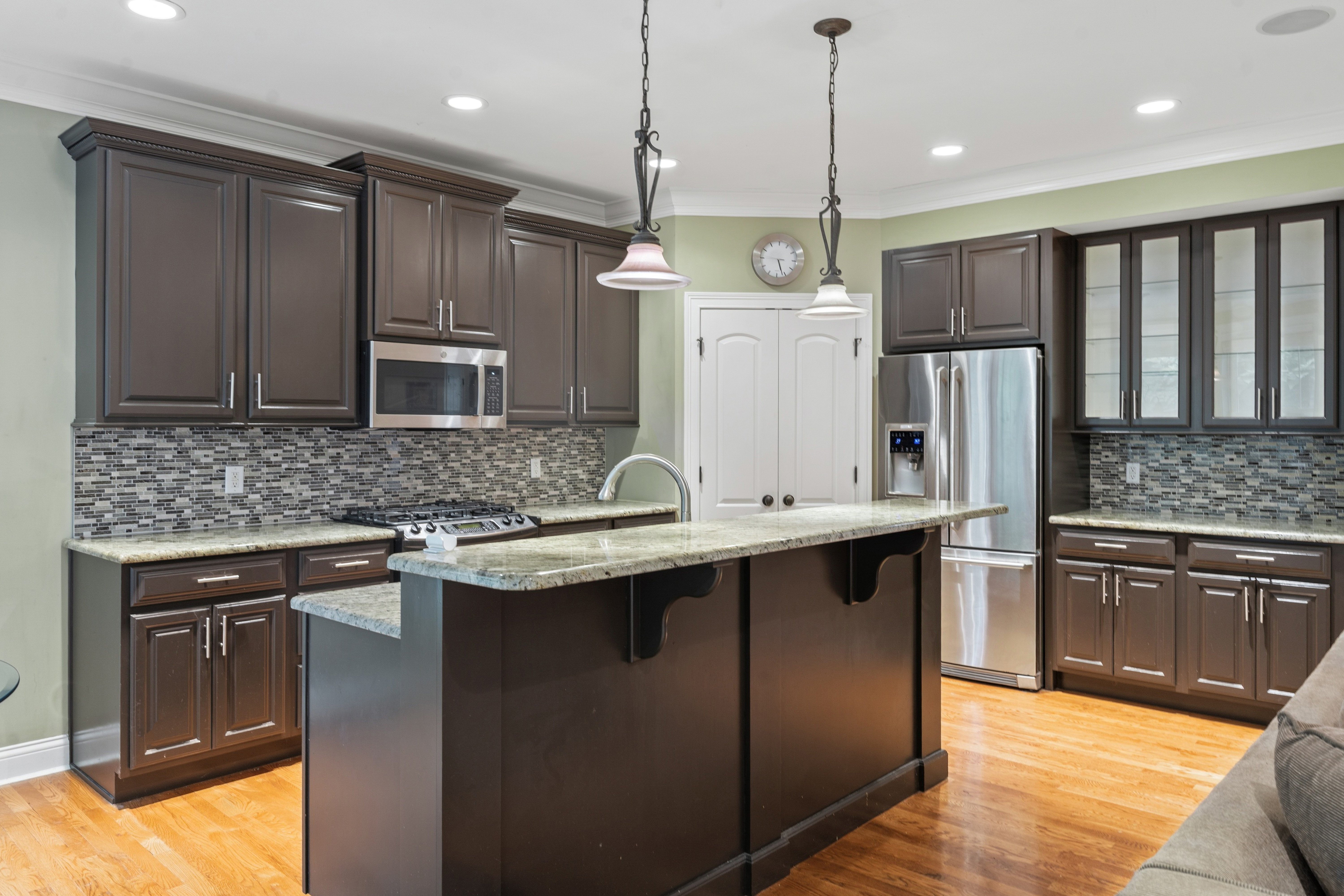 Kitchen with large dark island, pendant lights, granite counters, tile backsplash, and stainless appliances