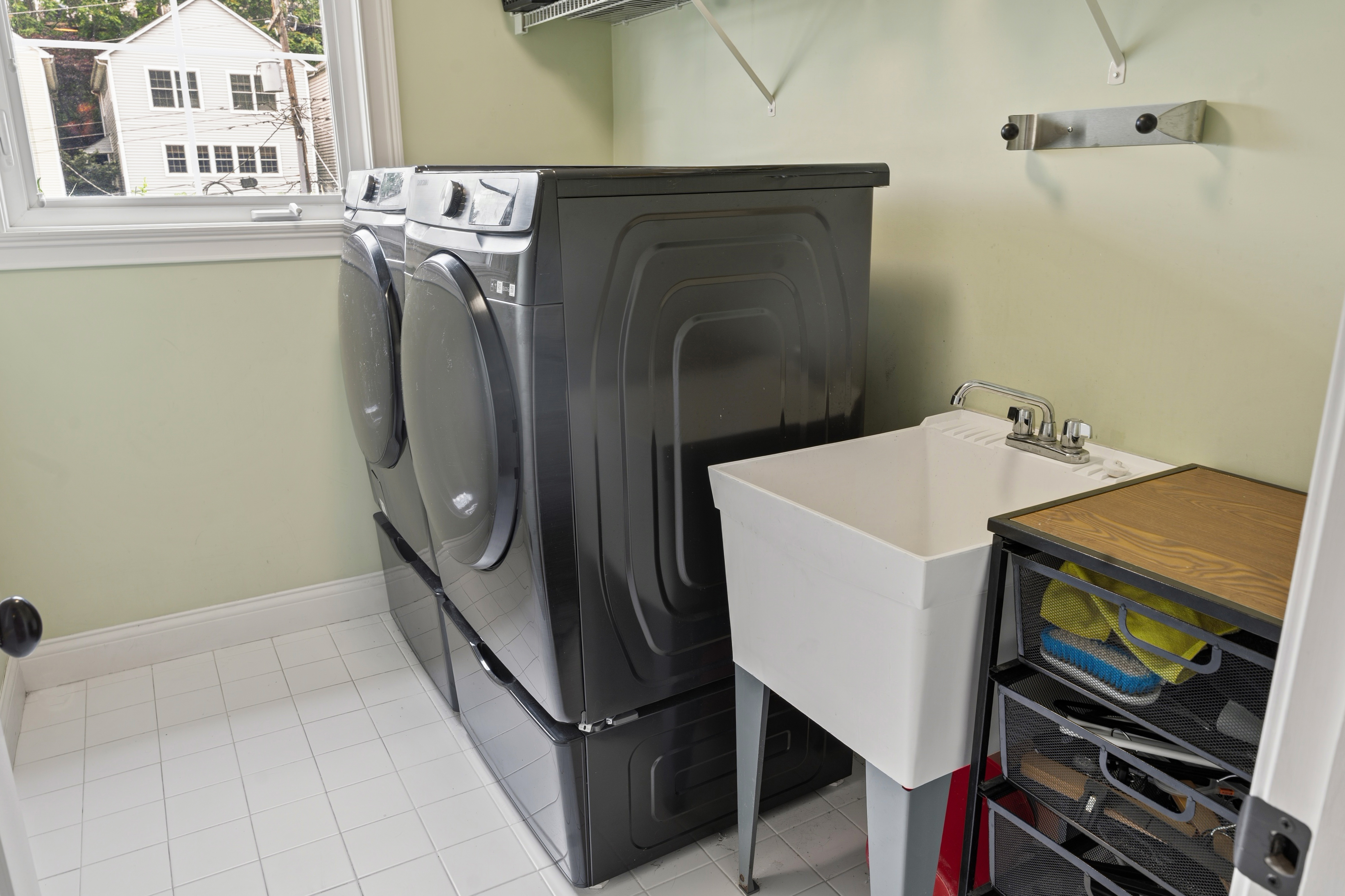 Laundry room with front-load washer and dryer on pedestals, utility sink, and window