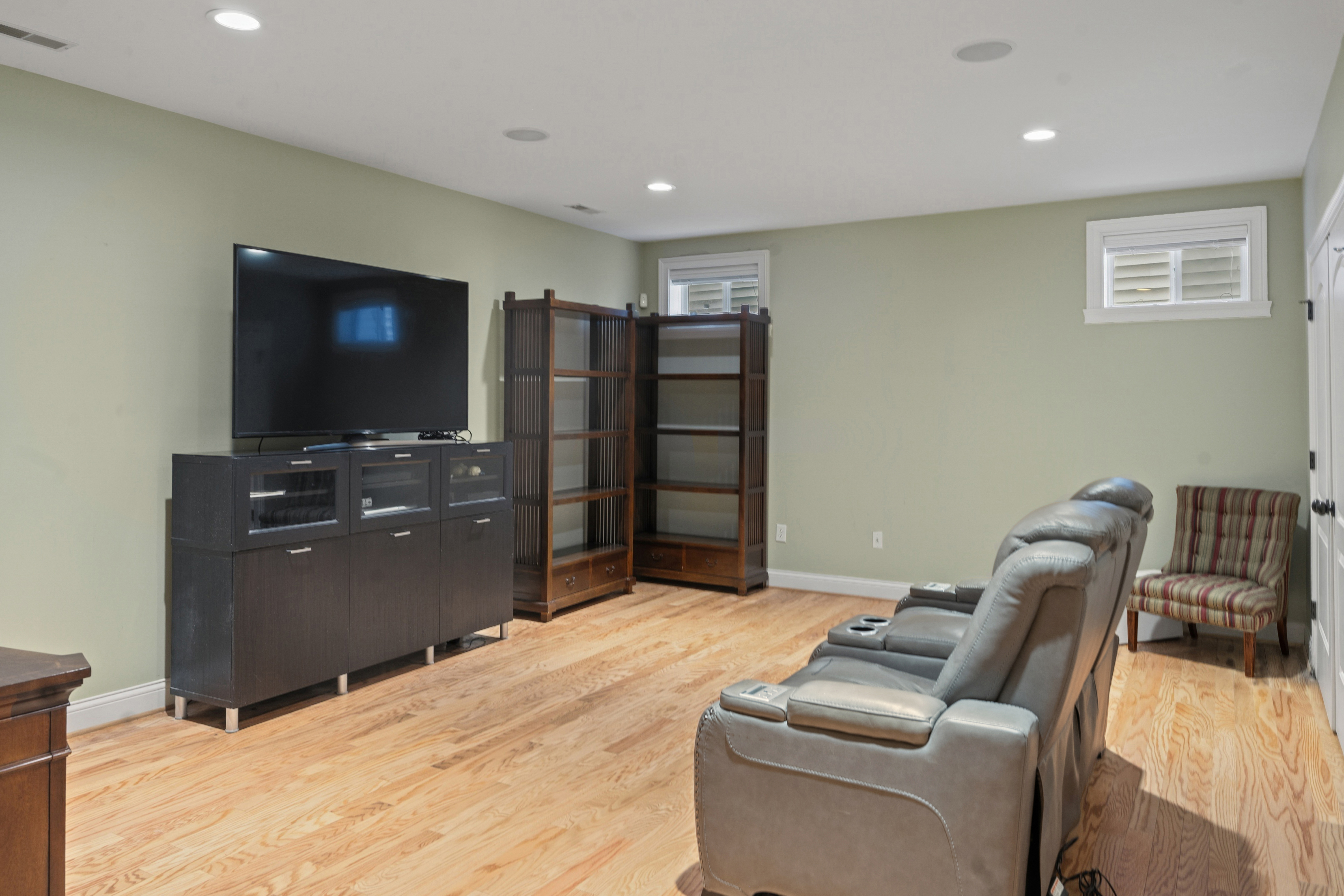 Lower level recreation room with leather recliners, large flat-screen TV, and media storage