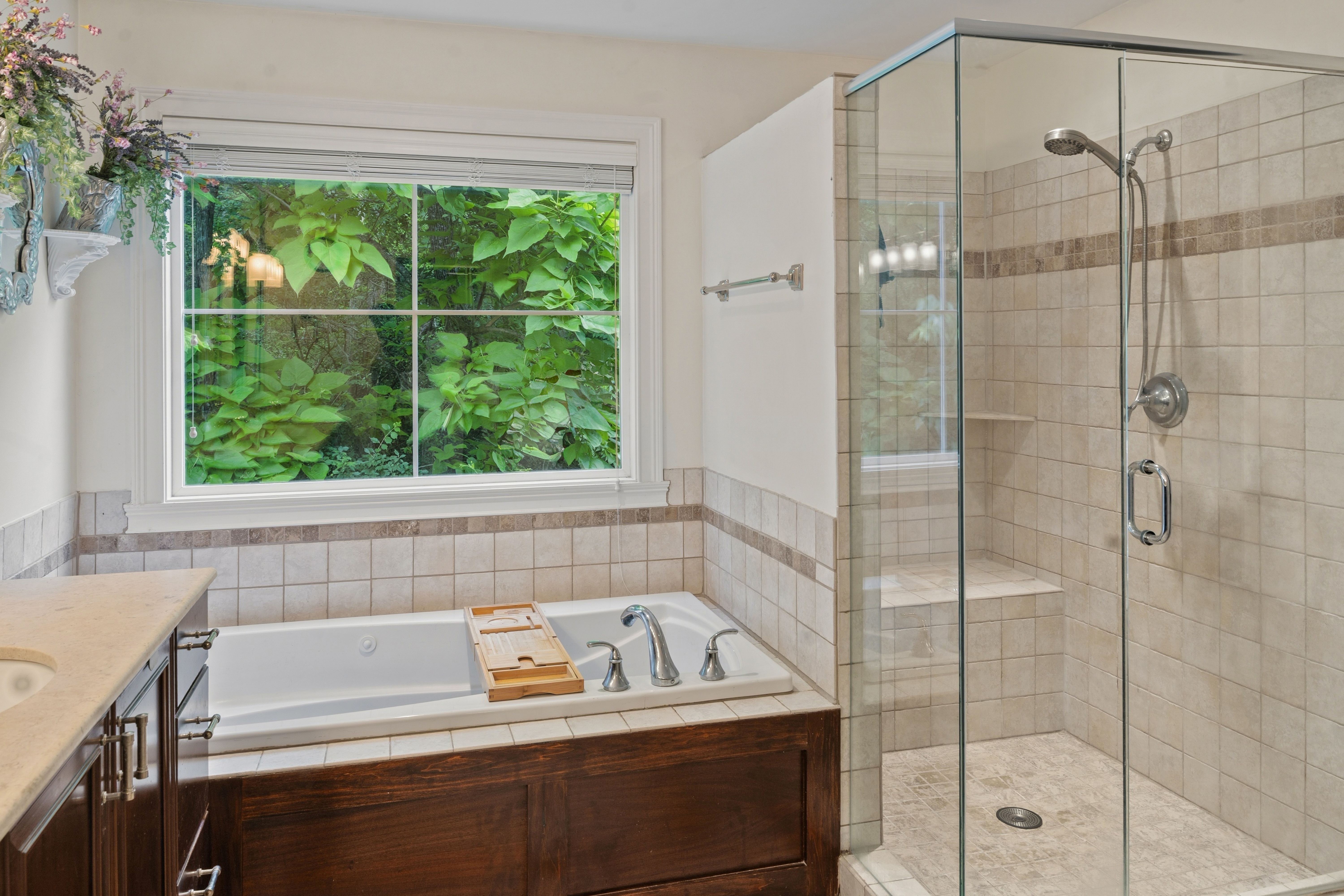 Primary bathroom soaking tub with garden window view and adjacent frameless glass shower