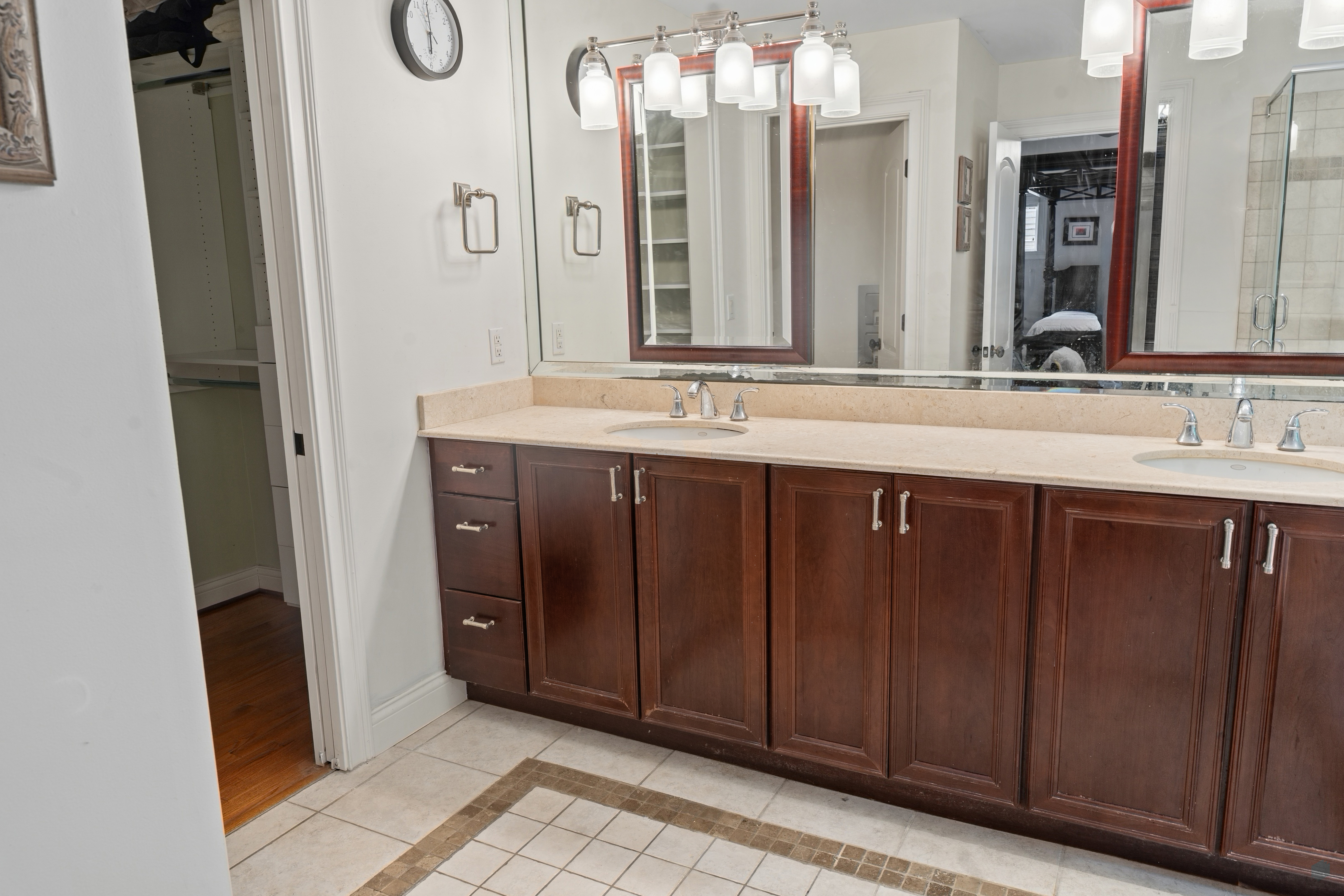 Primary bathroom double-sink vanity with dark wood cabinetry, stone countertop, and walk-in closet entry