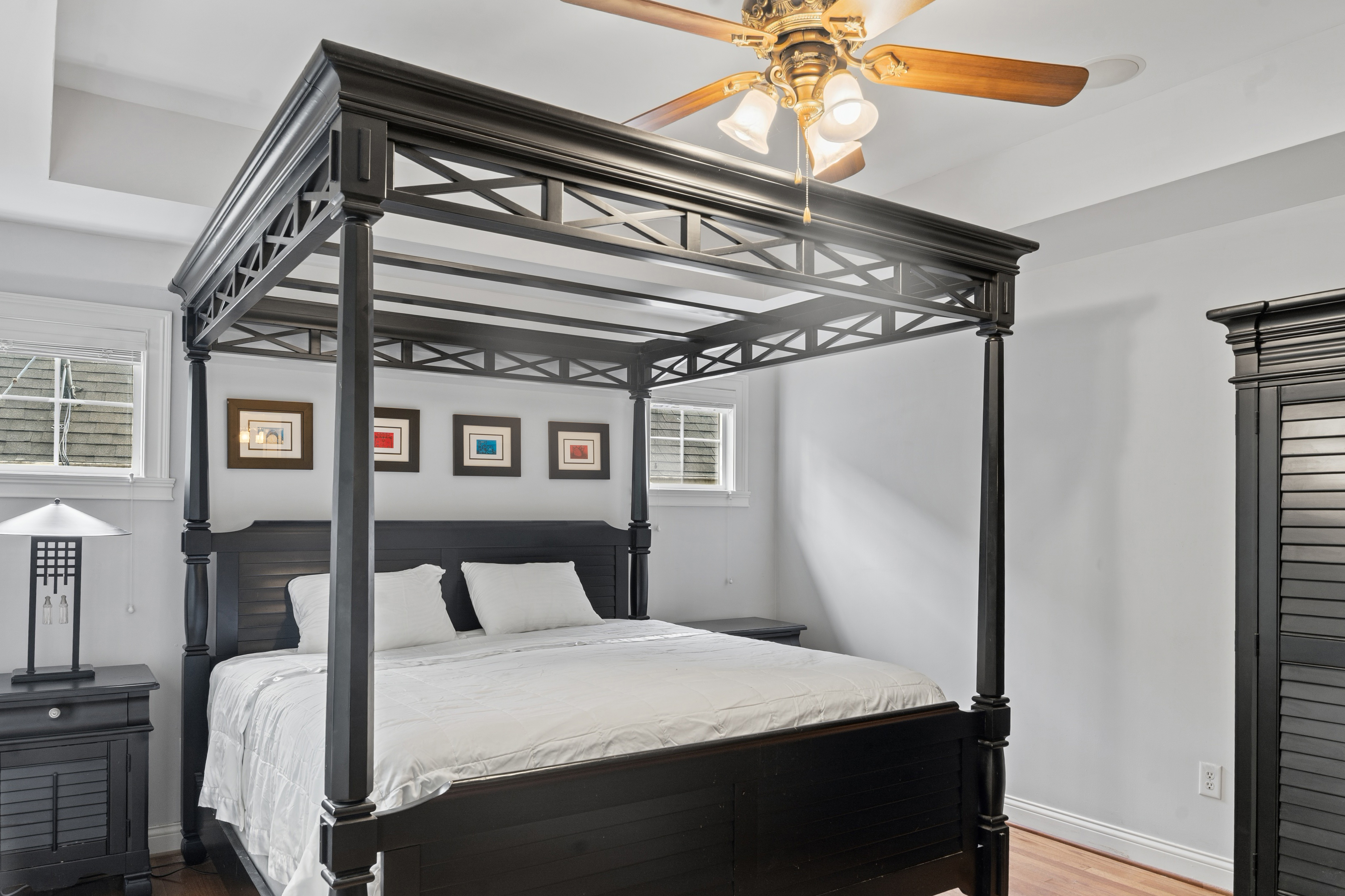 Primary bedroom with dramatic four-poster canopy bed, tray ceiling, ceiling fan, and shuttered windows