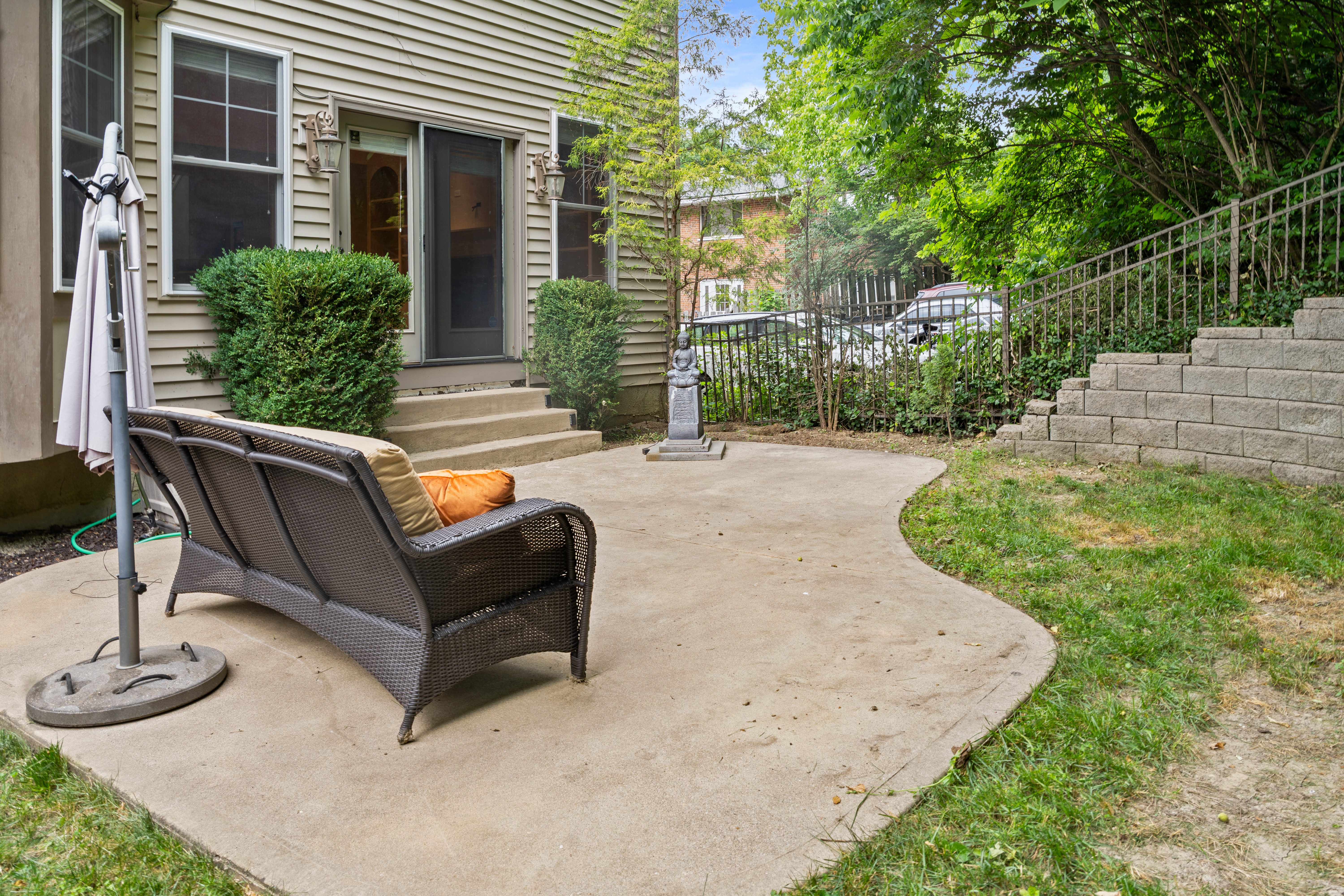 Rear patio with wicker outdoor seating, retaining wall steps, and mature backyard trees
