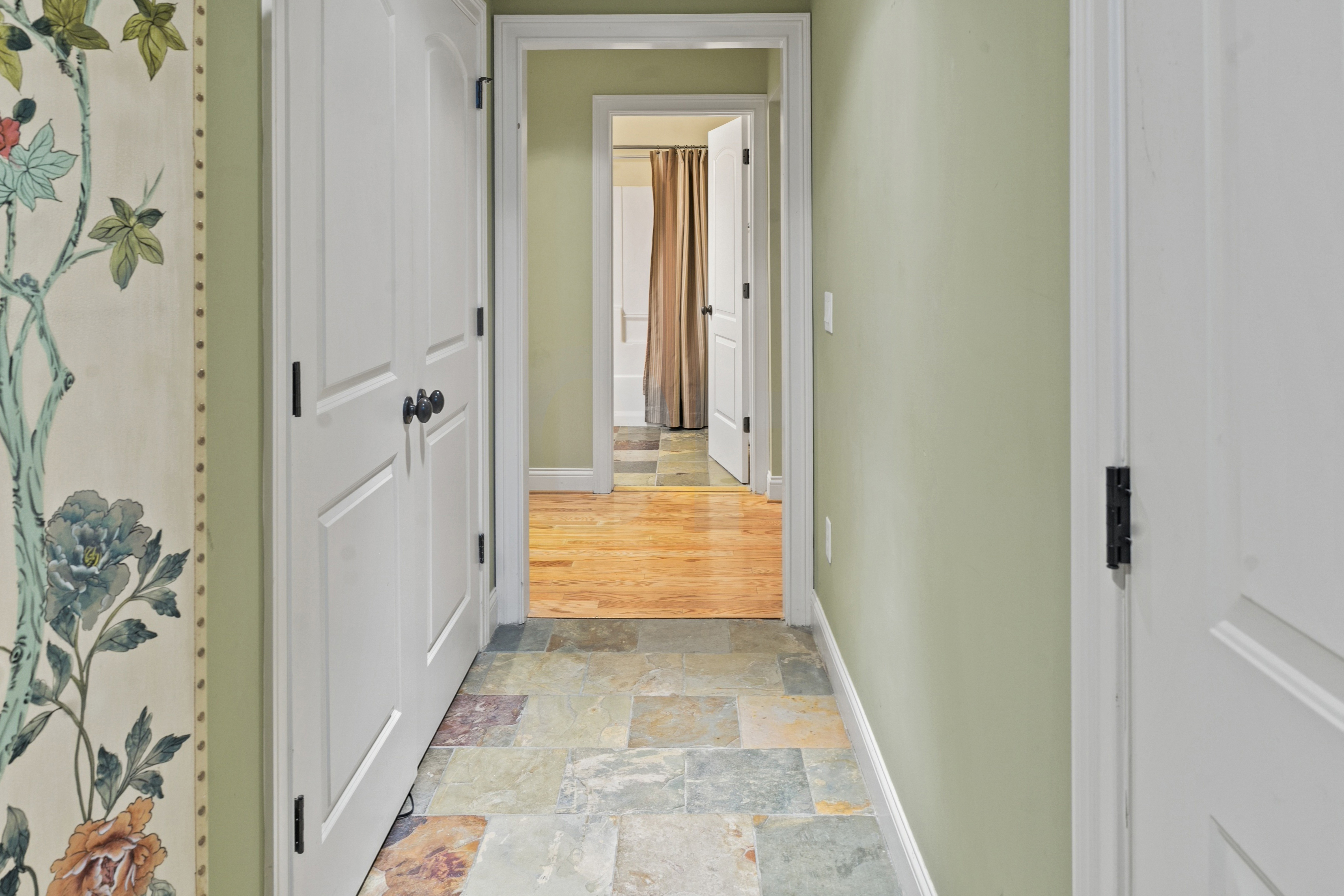 Second upper hallway with stone tile flooring, floral wallpaper accent wall, and bedroom views