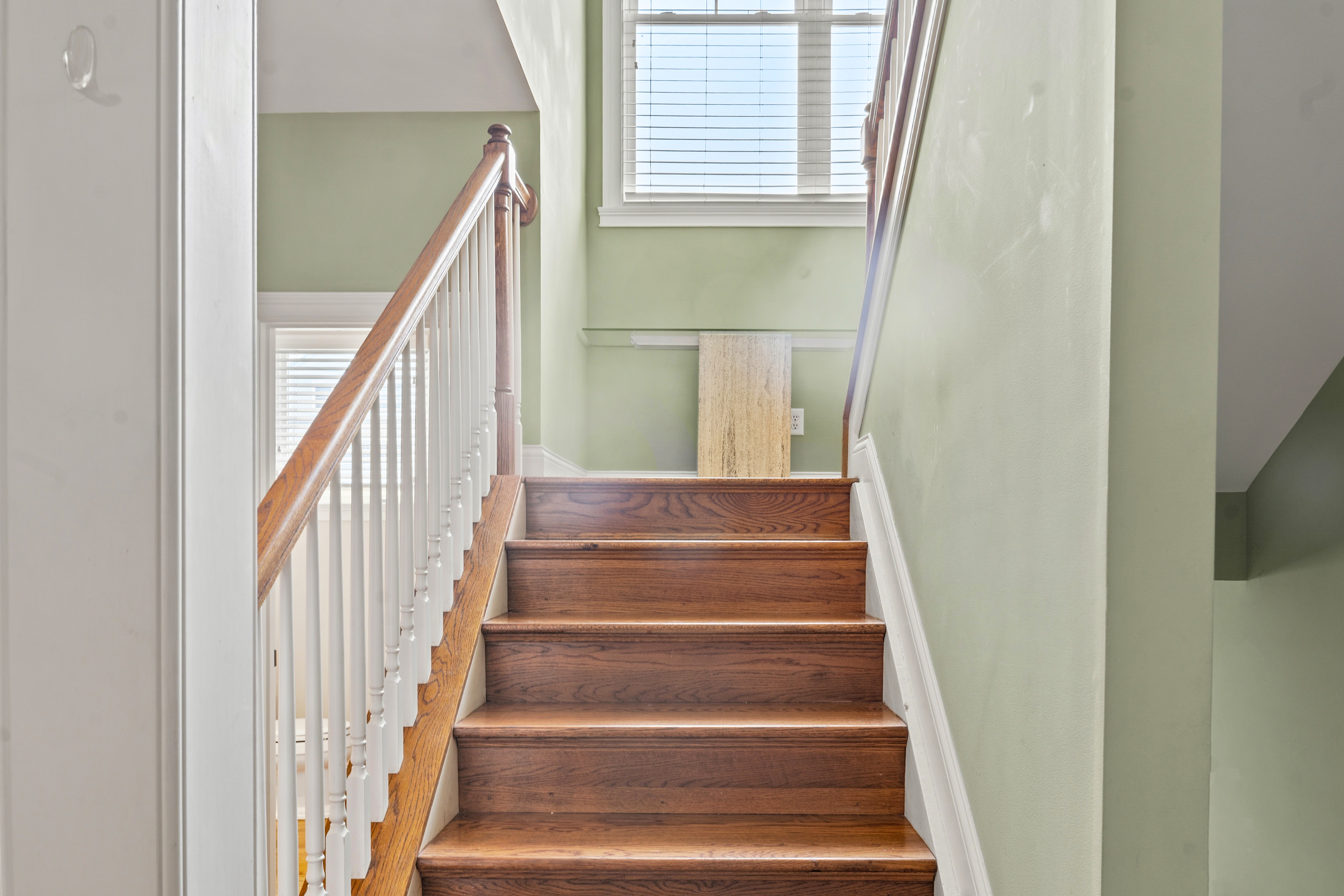 Upper staircase with wood treads, white spindles, and oak newel post leading to third floor