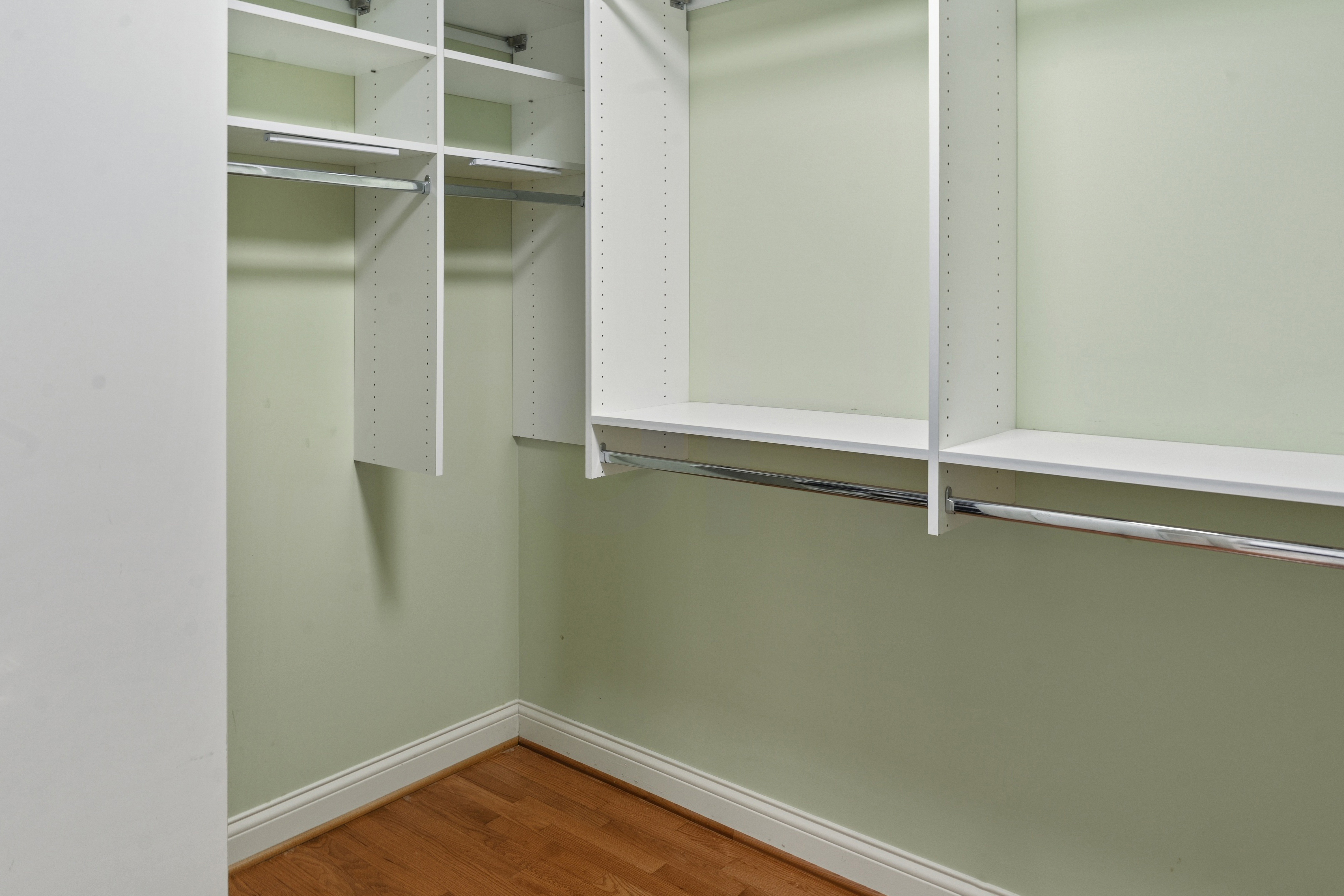 Walk-in closet corner with double hanging rods, adjustable shelving, and wood floors