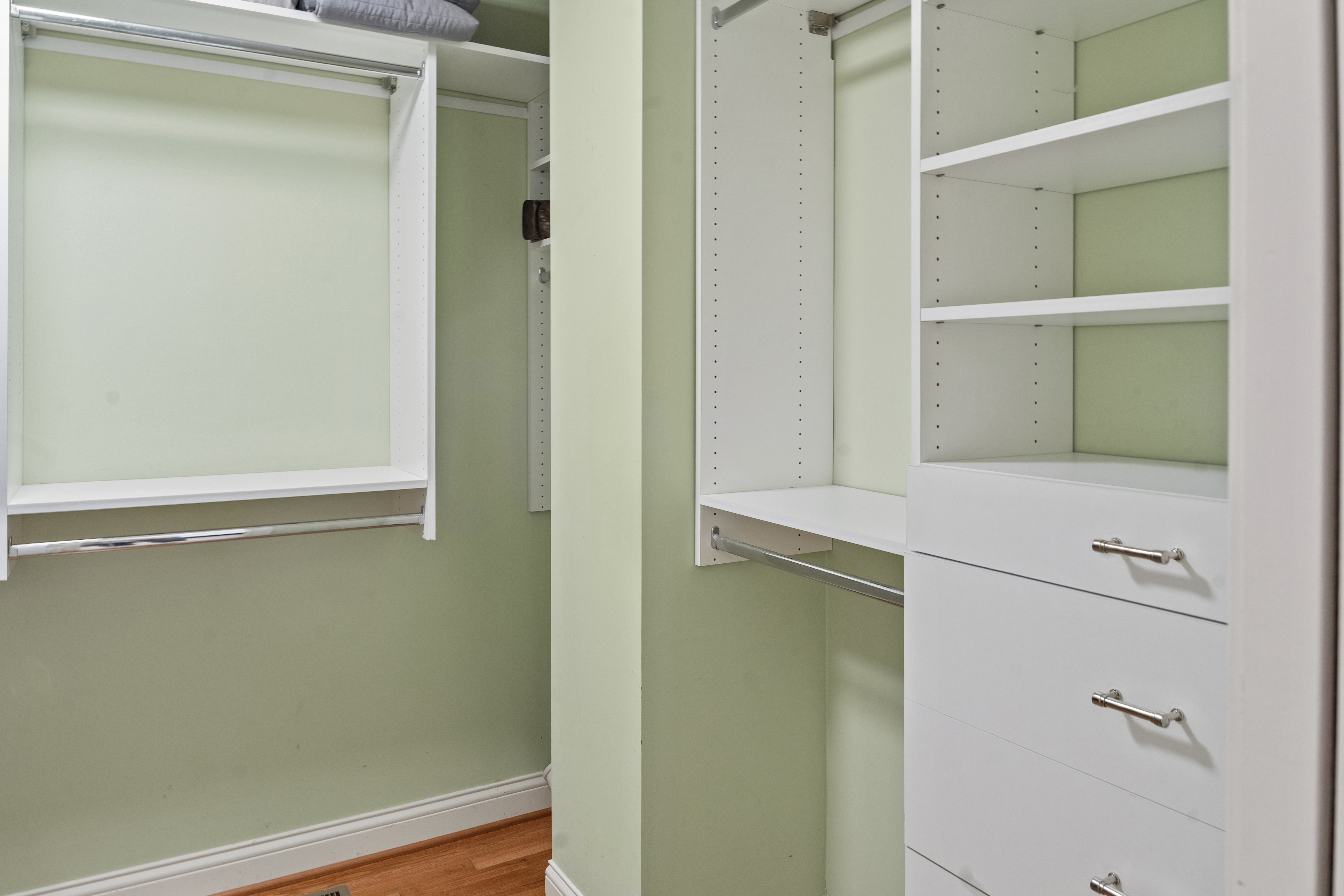 Walk-in closet with white built-in shelving, hanging rods, and drawers on hardwood floors