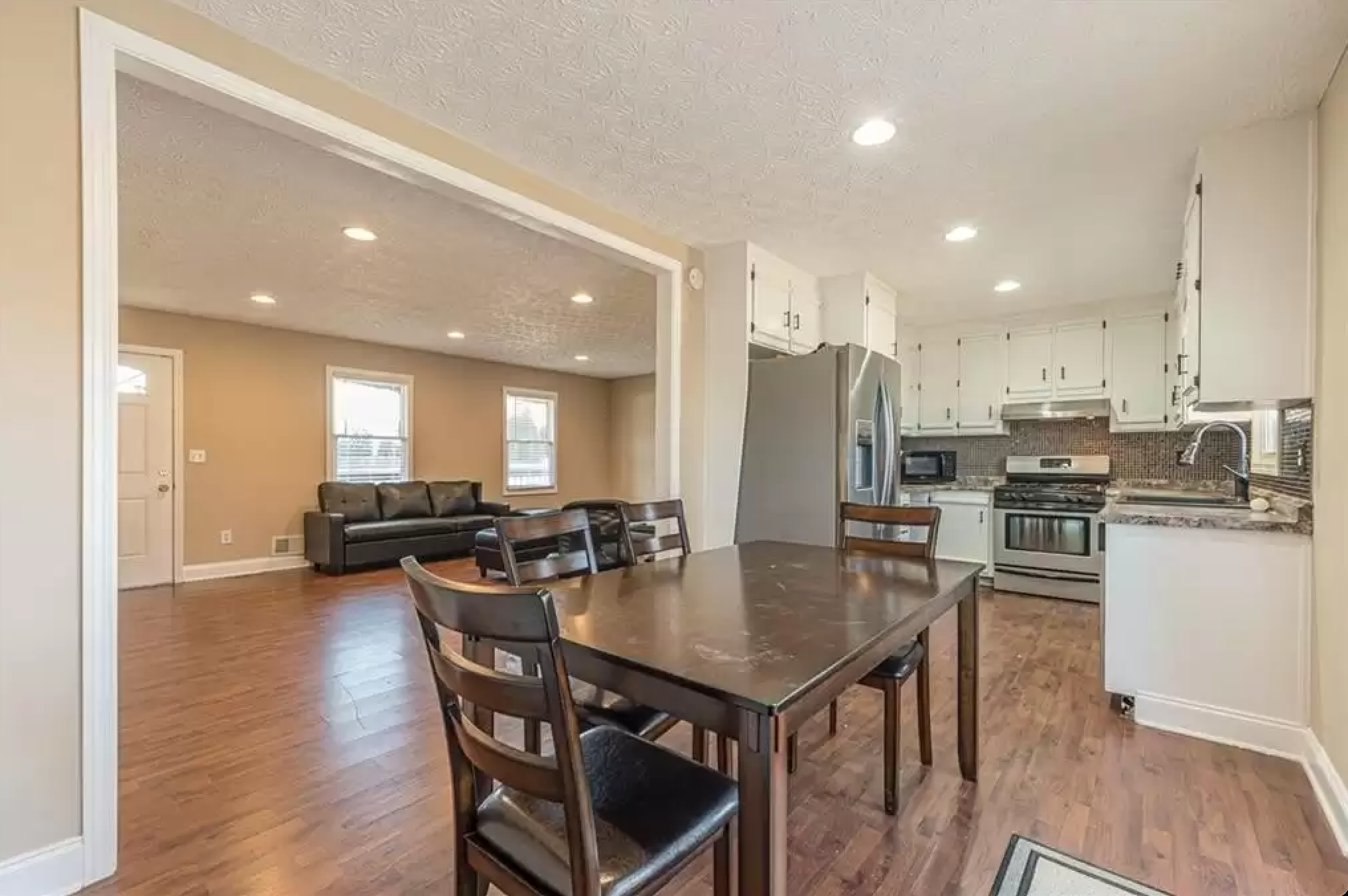 Dining area looking into kitchen and living room with table, stainless refrigerator, and white cabinetry