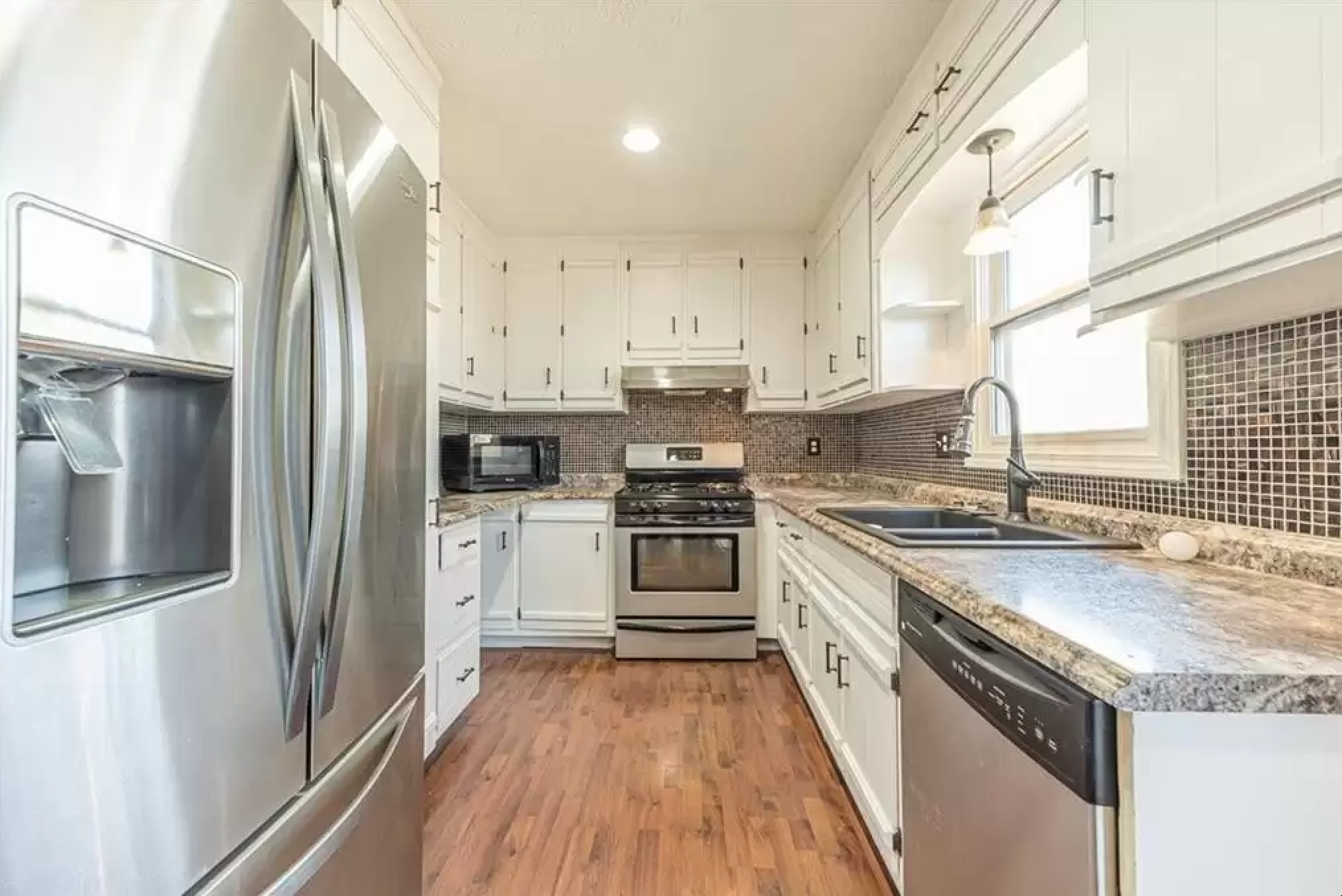 Galley kitchen with white cabinets, stainless appliances, granite counters, and tile backsplash