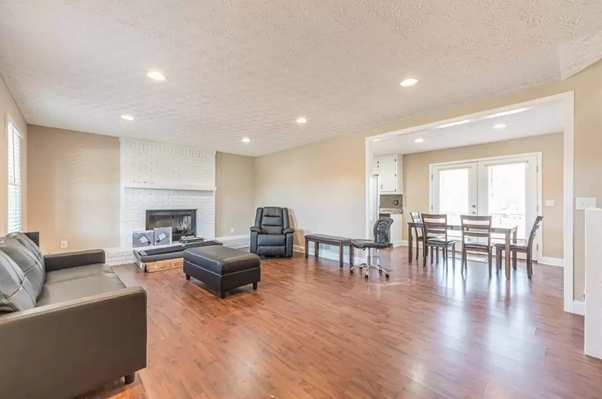 Open living and dining area with kitchen sightline, white fireplace, and wood flooring