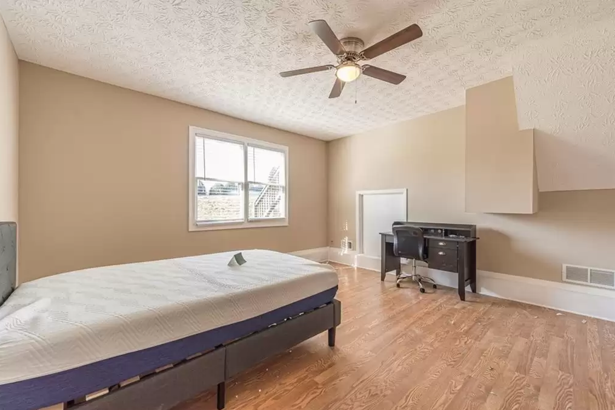 Secondary room with wood flooring, ceiling fan, window, desk, and neutral walls